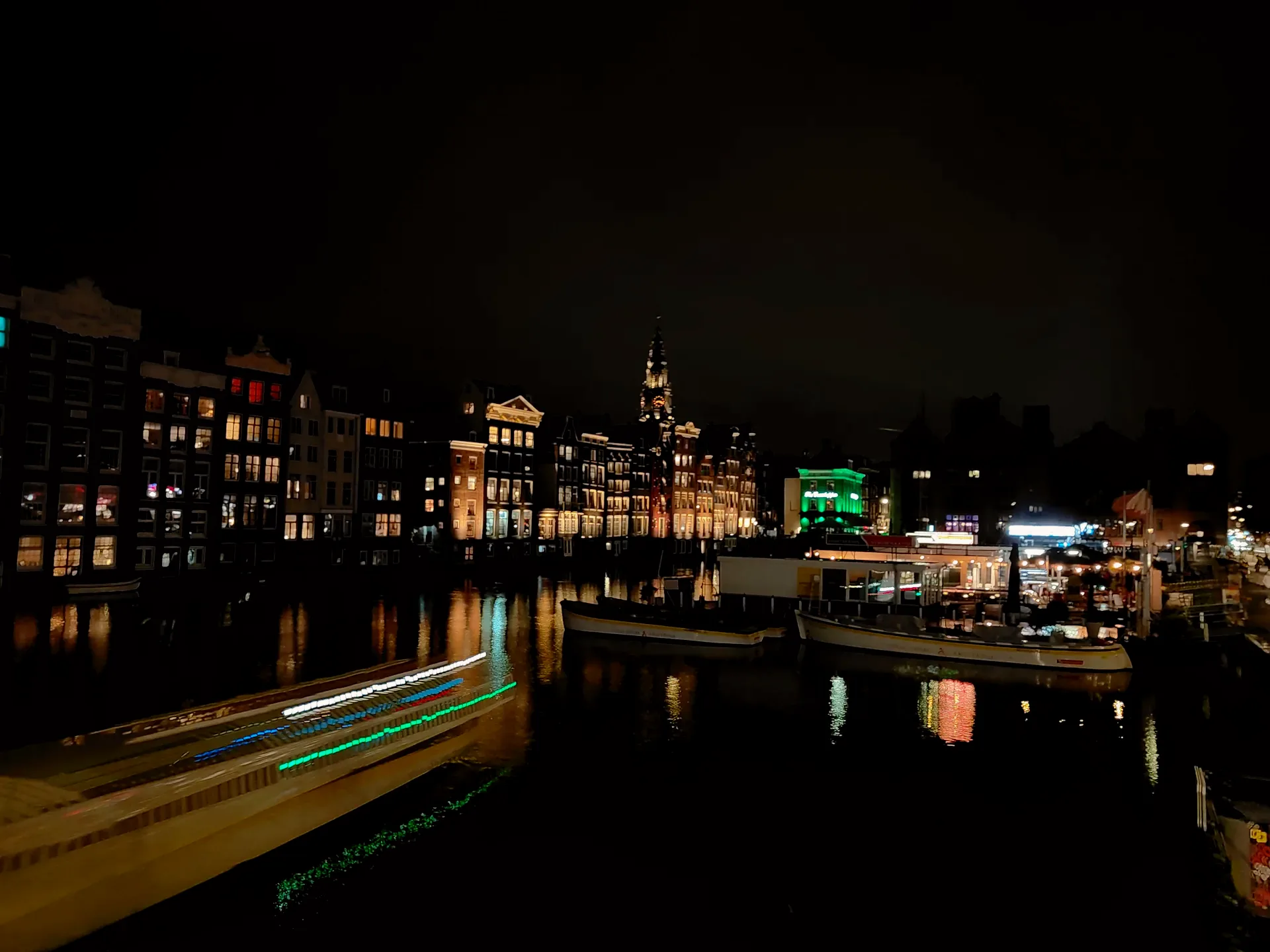 a long-exposure boat light trail down the damrak at night, gabled houses lit on the water