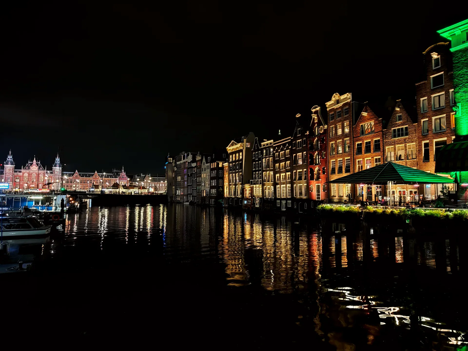 the Damrak houses glowing over the canal at night, Centraal beyond