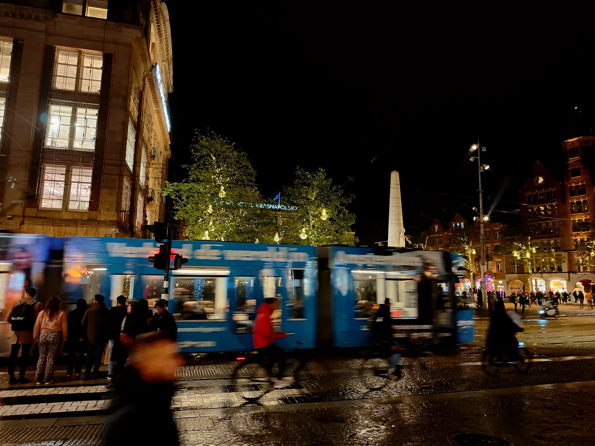 a blue tram past the monument on dam square