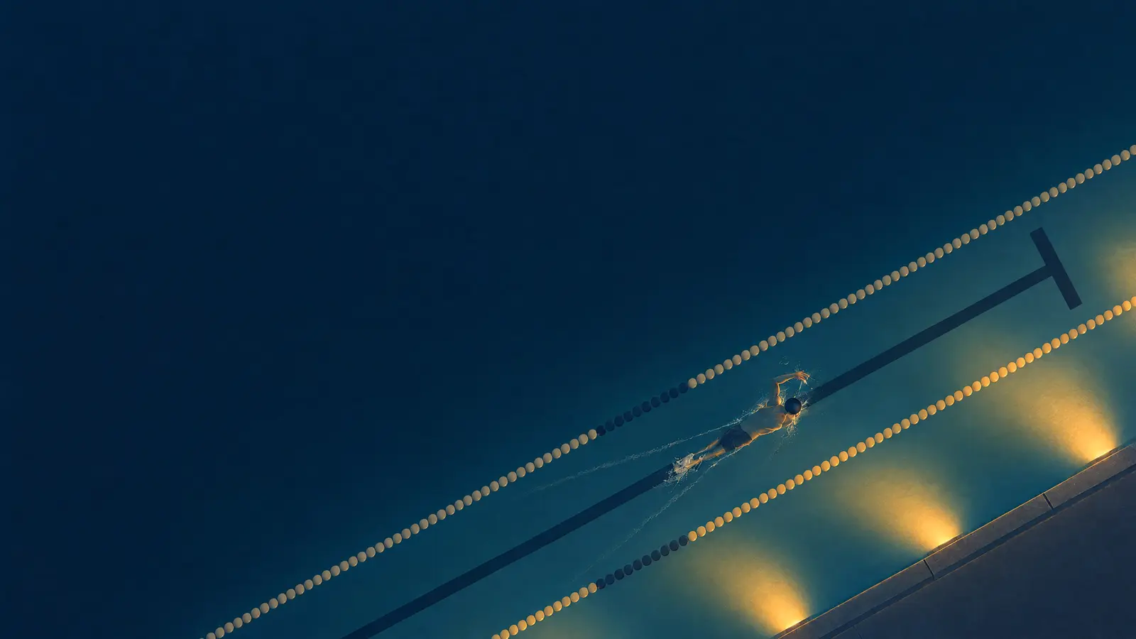 Illustration of a pool at night seen from straight above with someone swimming freestyle and underwater lights glowing in the pool wall.